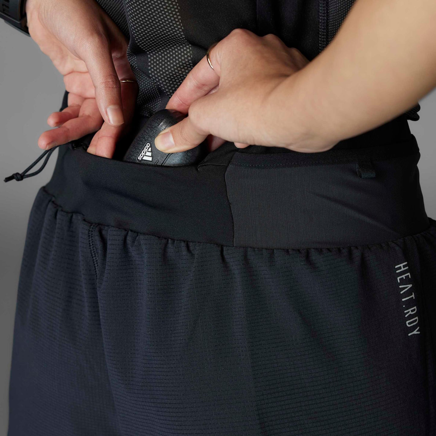 Person adjusting a black adidas shoe in a pocket of dark pants with 'HEATRDY' branding.