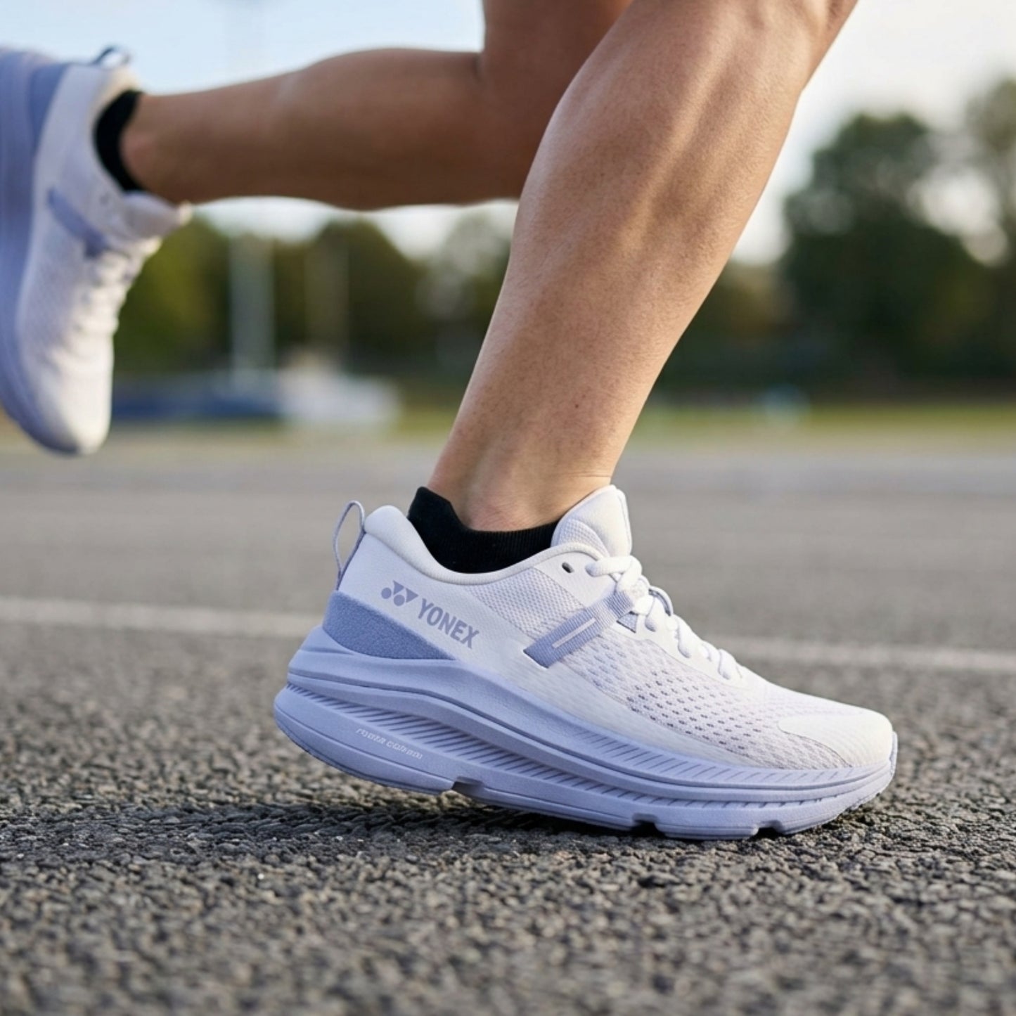 Person wearing white running shoes with Yonex logo on a track