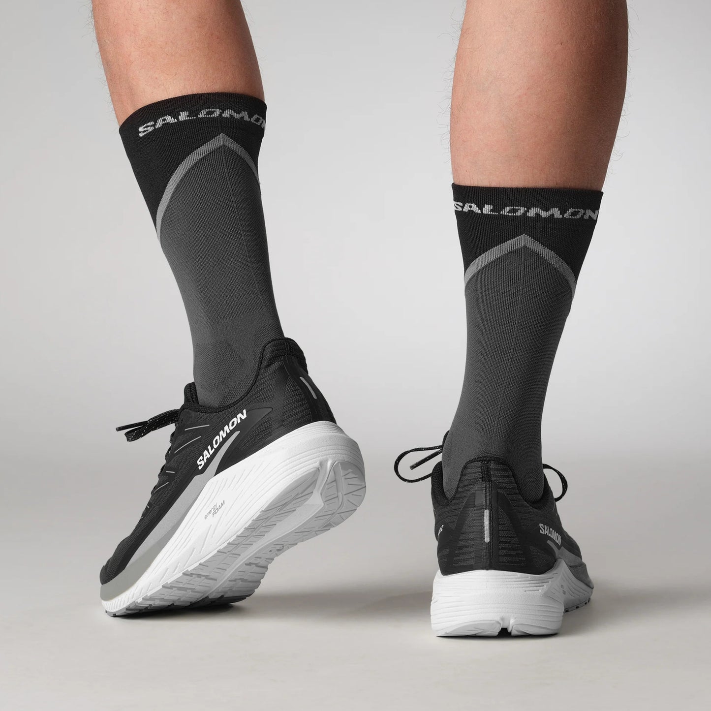 Person wearing black Salomon running shoes and socks on a light gray background