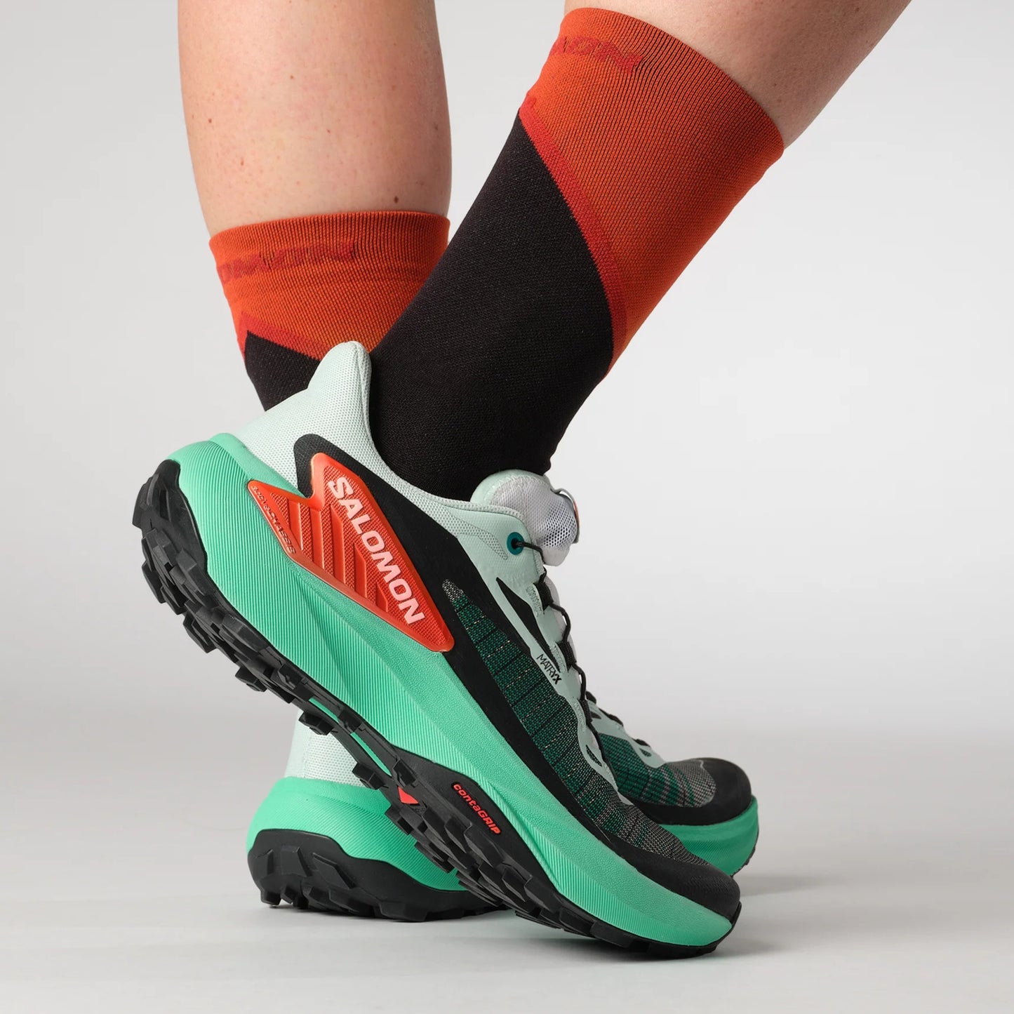 Green Salomon running shoes with black and red accents worn by a person on a light gray background