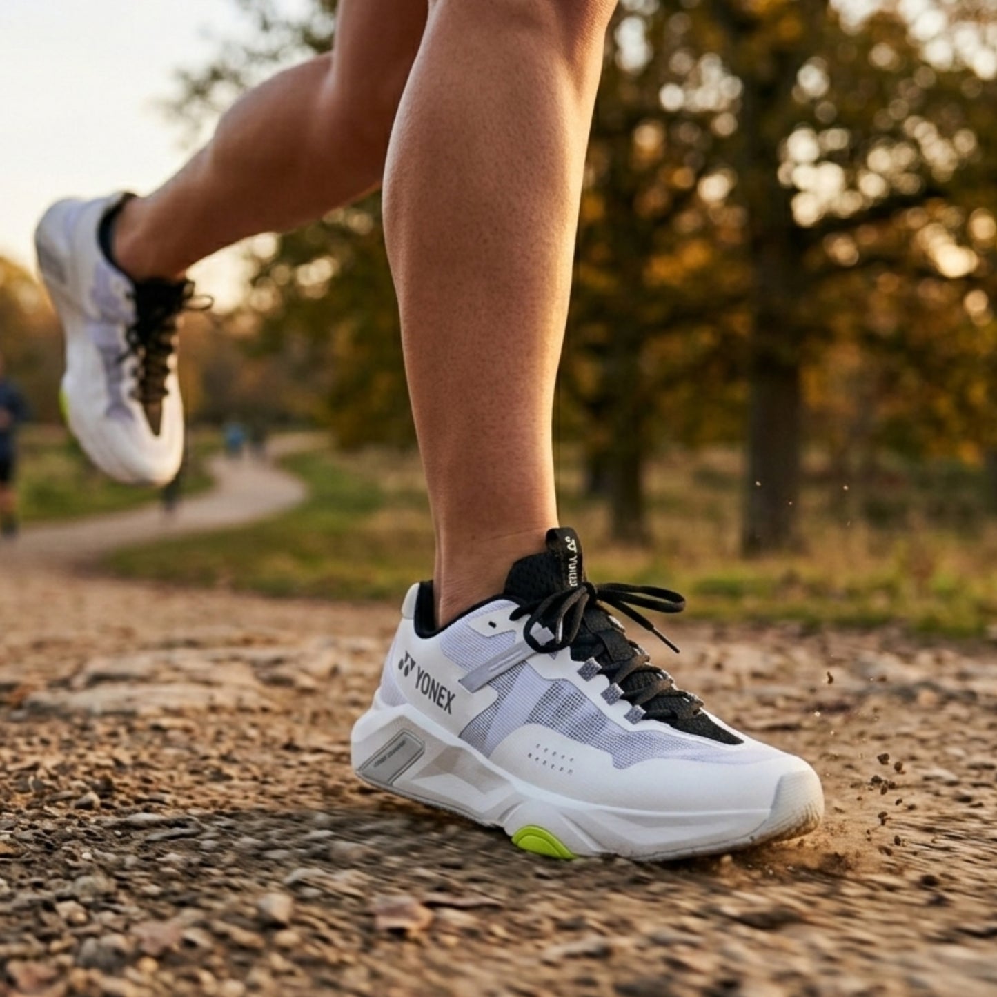 Person running outdoors wearing white Yonex running shoes with black laces and green accents.