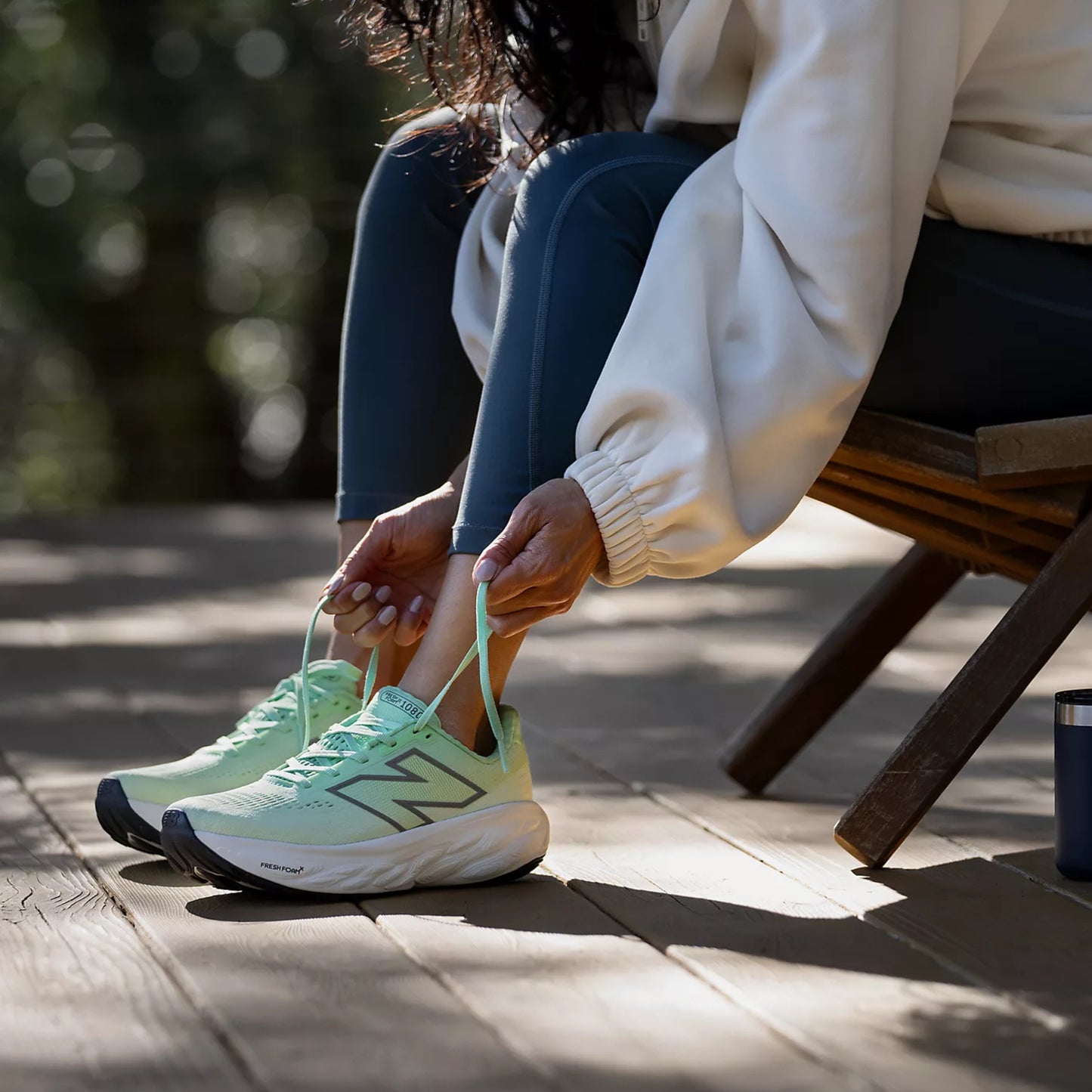 Person tying light green running shoes on a wooden bench outdoors