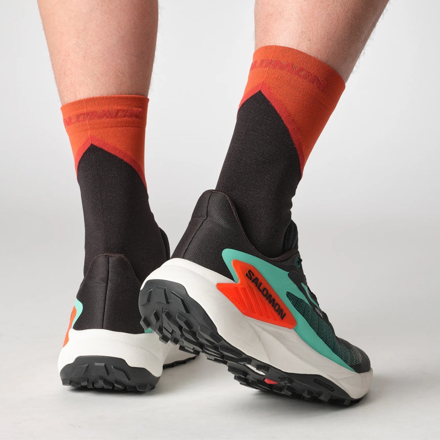 Black and green Salomon running shoes with orange accents on a neutral background