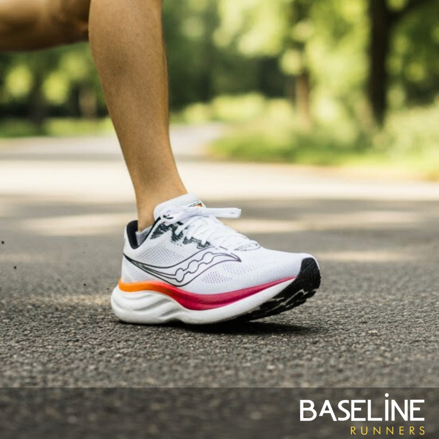 White Saucony running shoe with colorful sole on a road, blurred greenery in the background, featuring 'Baseline Runners' brand.