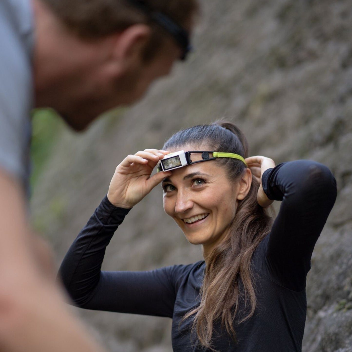 Woman adjusting a headlamp outdoors with a mountainous background