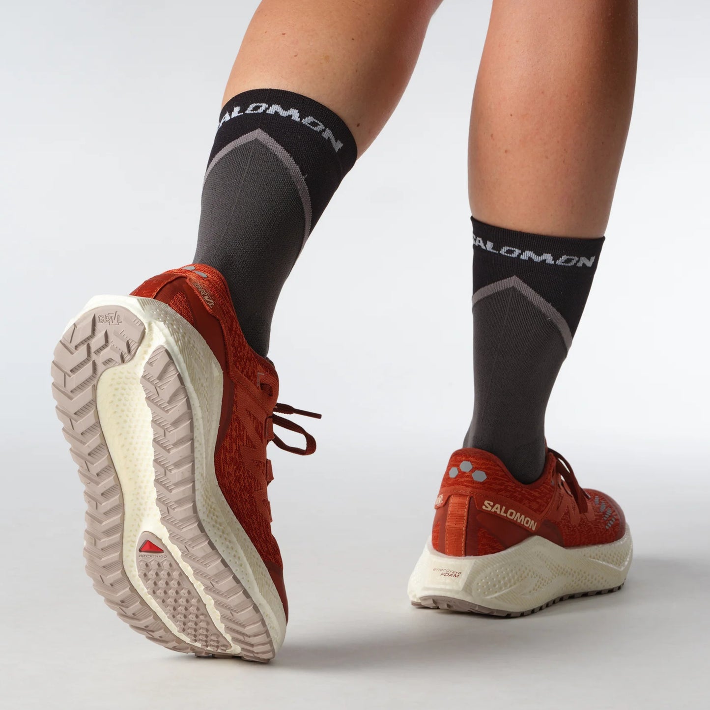 Red Salomon running shoes with white soles and black socks featuring Salomon branding on a light gray background.