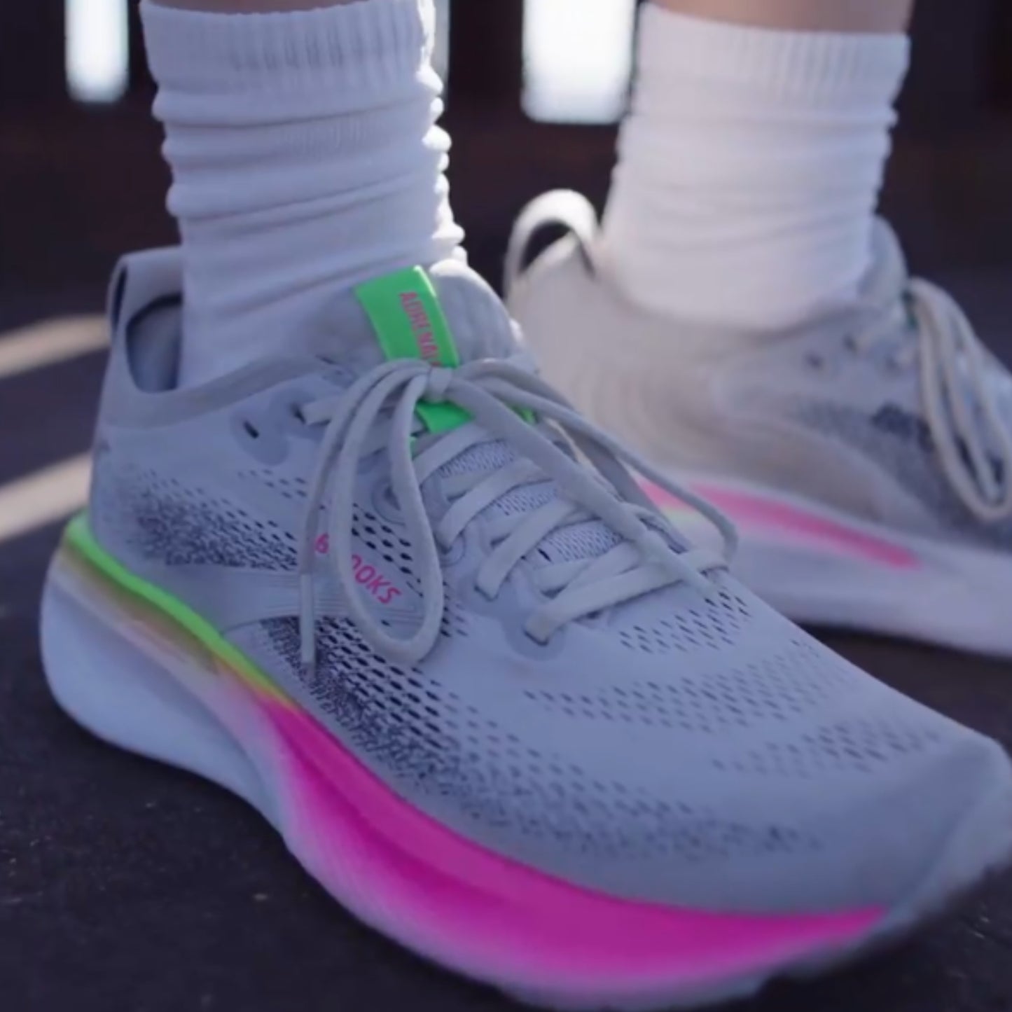 Gray Brooks running shoe with pink sole and green accents on a dark surface