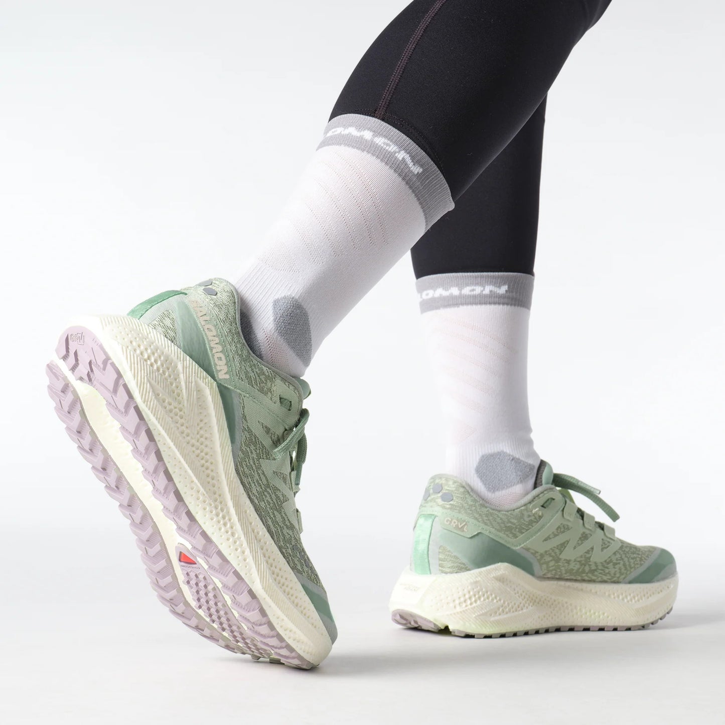 Light green Salomon running shoes worn with black leggings and white socks on a light gray background