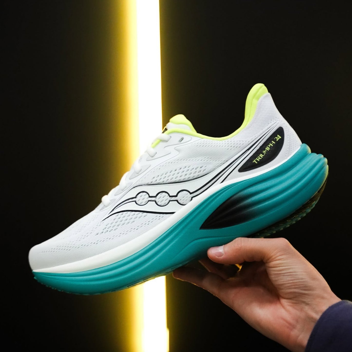 White and teal Saucony running held by a hand against a dark background