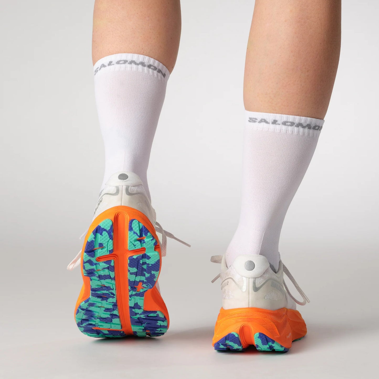 White running shoes with colorful soles and white socks on a light gray background