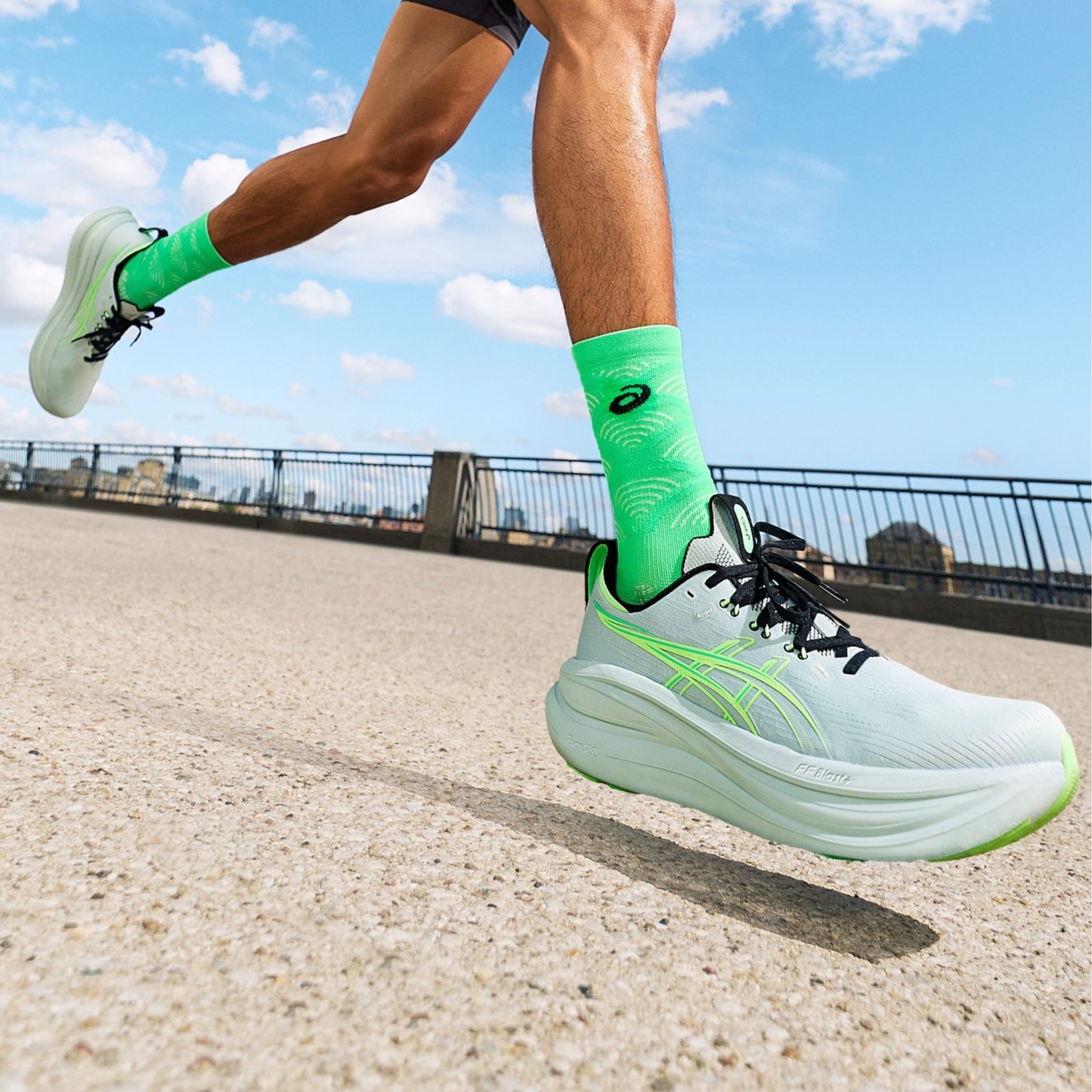 Person running on a road with green Asics running shoes and socks against a blue sky.