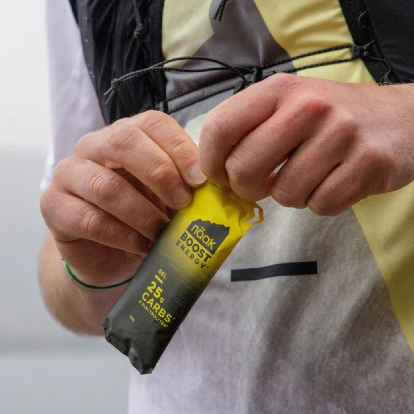Person holding a yellow energy bar with 'naak boost energy' branding.