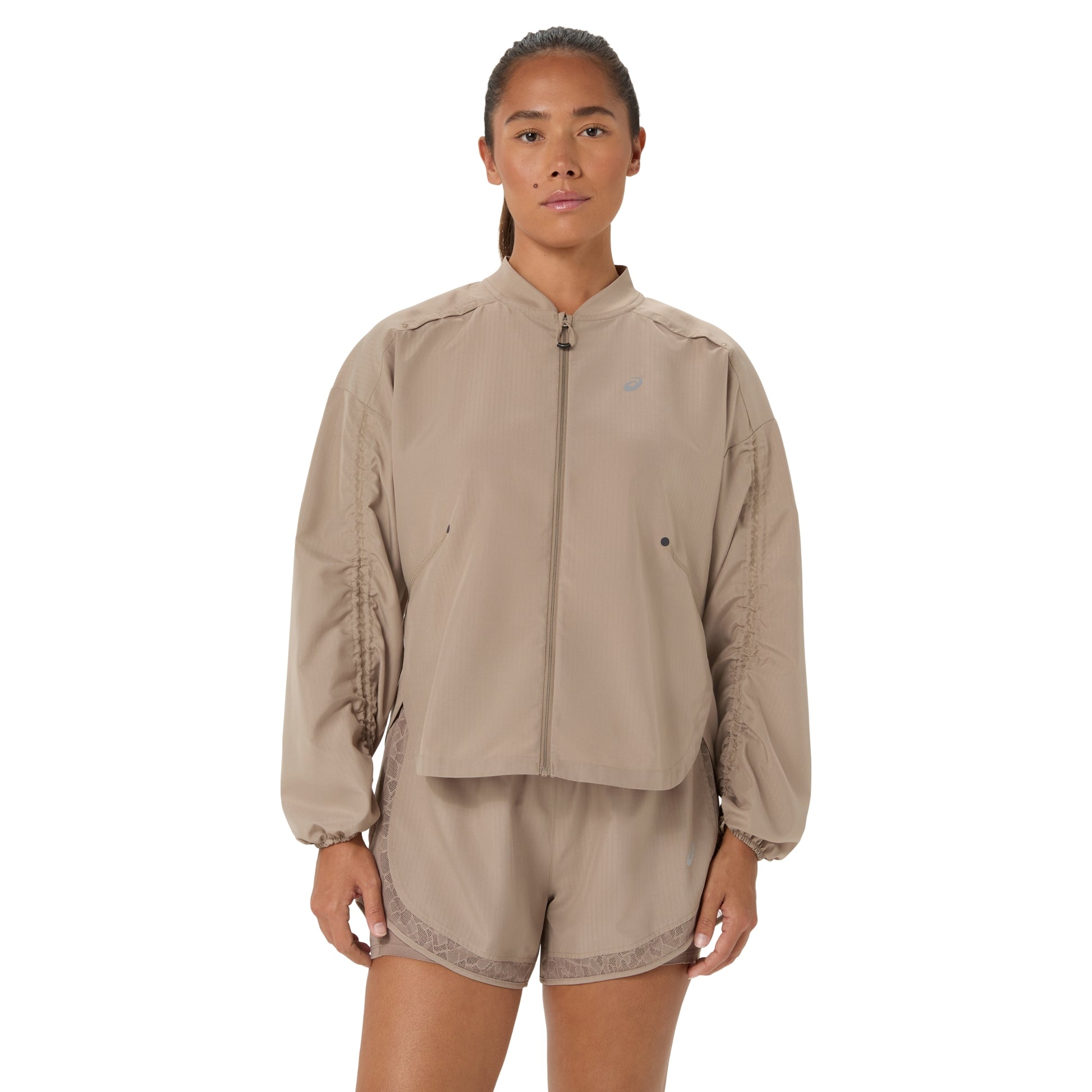 A model wearing a beige zip-up jacket and matching shorts set against a plain white background.