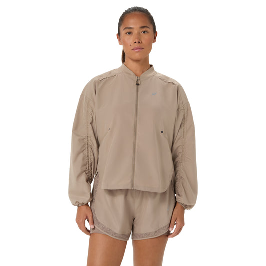 A model wearing a beige zip-up jacket and matching shorts set against a plain white background.