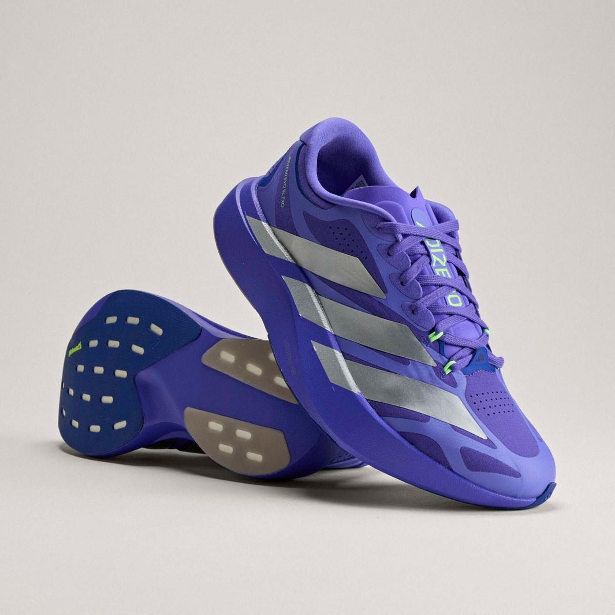 A pair of Adidas running shoes in a vibrant purple and blue colorway, featuring silver side stripes and a textured sole, photographed on a neutral light gray background.