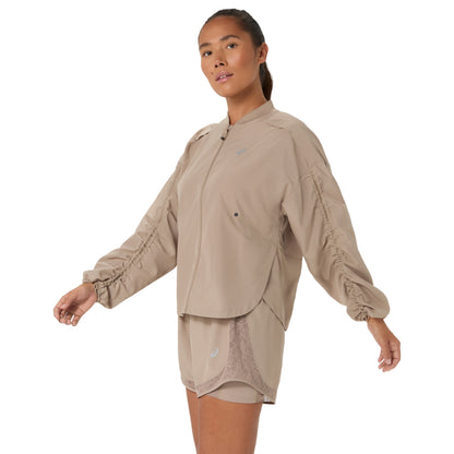 A woman modeling a light beige athletic jacket and matching shorts set against a plain white background.