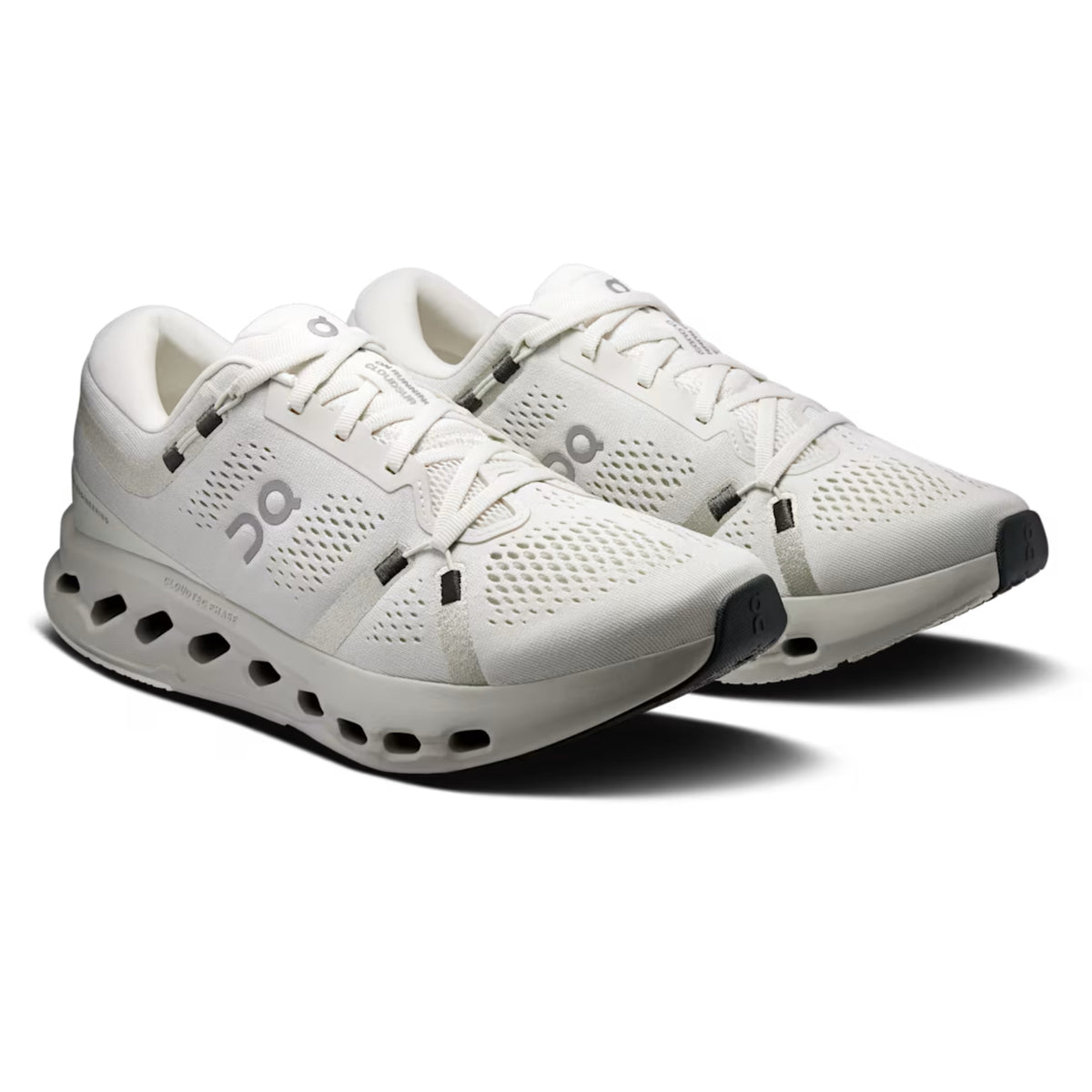A pair of On running shoes in off-white and light gray, featuring a breathable mesh upper, cushioned midsole with visible air holes, and black accents on the toe caps and laces, set against a plain white background.