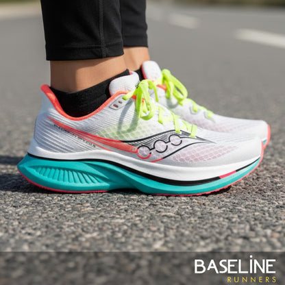 White running shoe with colorful sole on a road, featuring the Saucony brand.