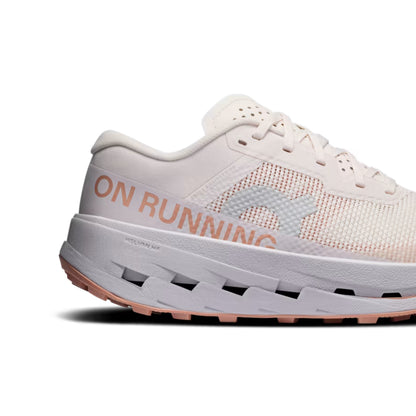 A close-up side view of a On running shoe in off-white with peach-pink accents and the word 'ON RUNNING' printed on the side, set against a plain white background.