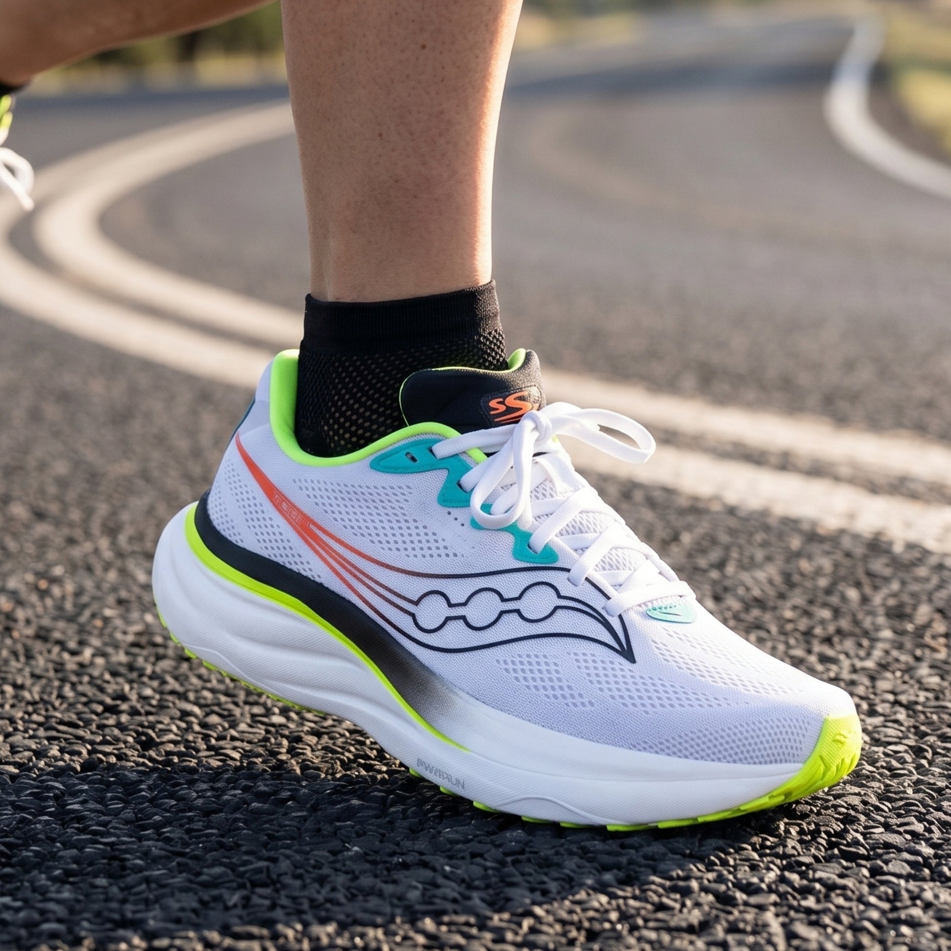 Person wearing a hite and black running shoe with yellow accents on a road 