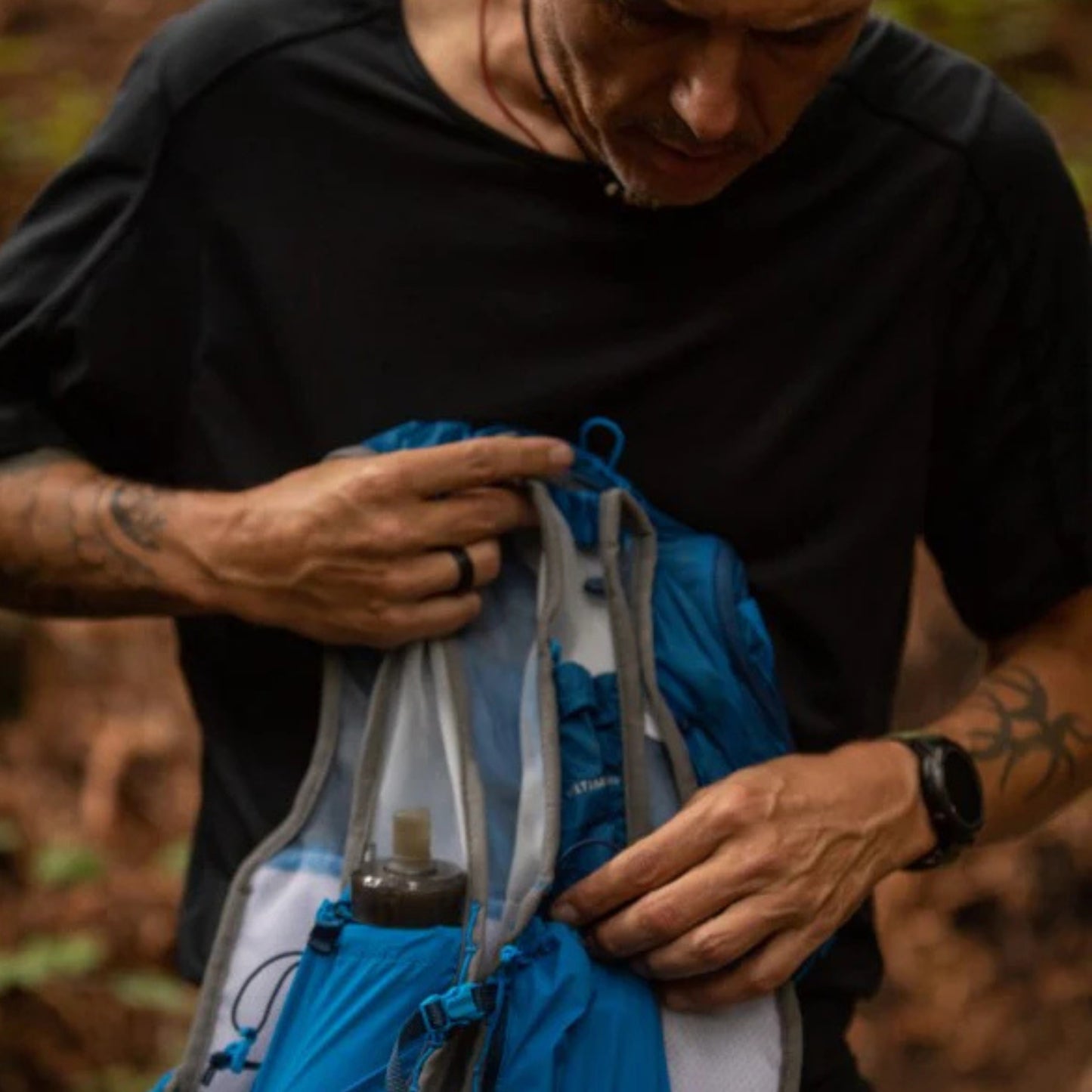 Person holding a blue and gray hydration pack with a water bottle inside, outdoors.