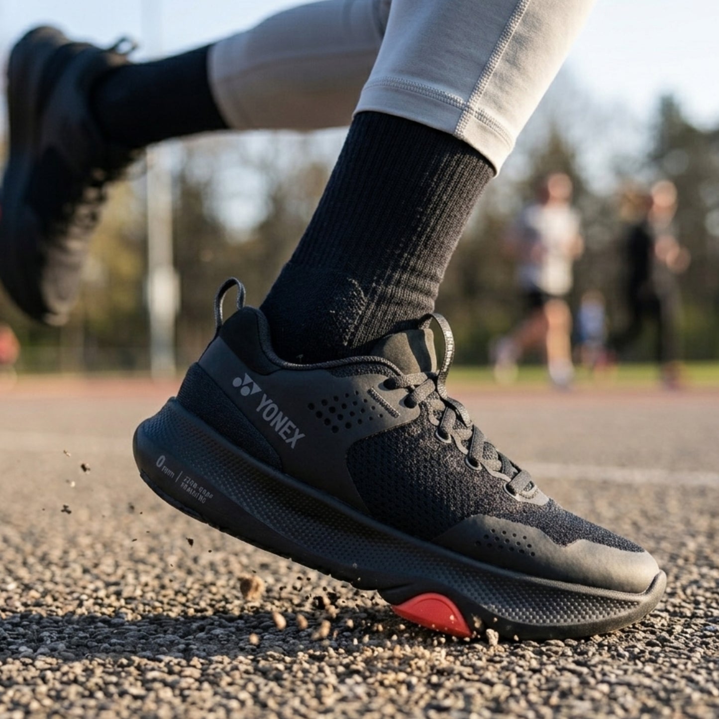 Black Yonex running shoe with red sole on a track, featuring Yonex branding.