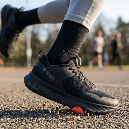 Black Yonex running shoe with red sole on a track, featuring Yonex branding.