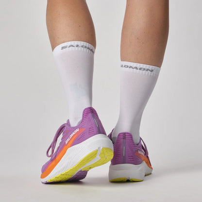 Purple Salomon running shoes with orange accents worn with white socks on a light gray background