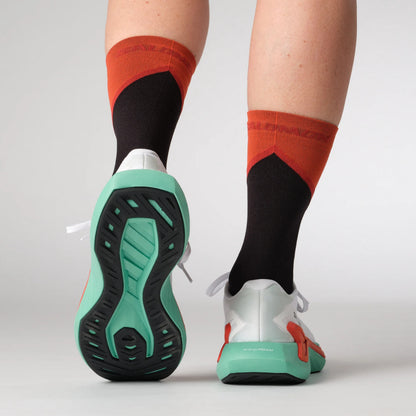 Person wearing red and black socks with white Salomon running shoes on a light gray background