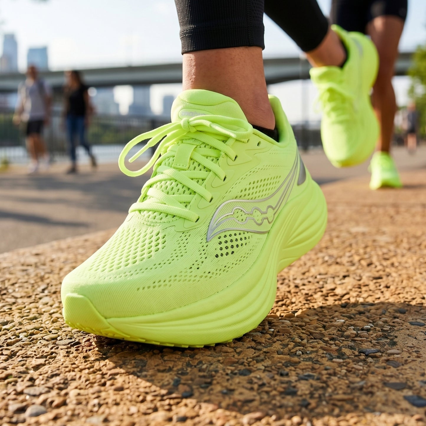 Nenon green Saucony running shoes with a visible brand logo on a road with people in the background.