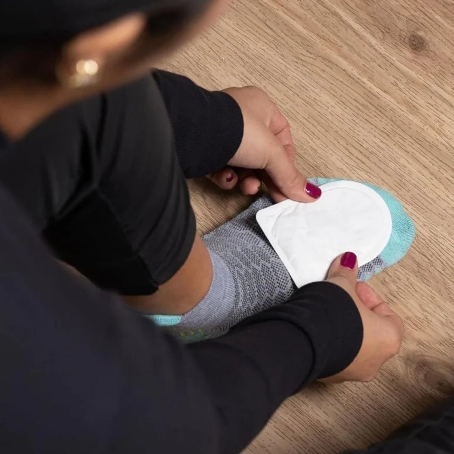 Person applying a white patch to their foot on a wooden floor