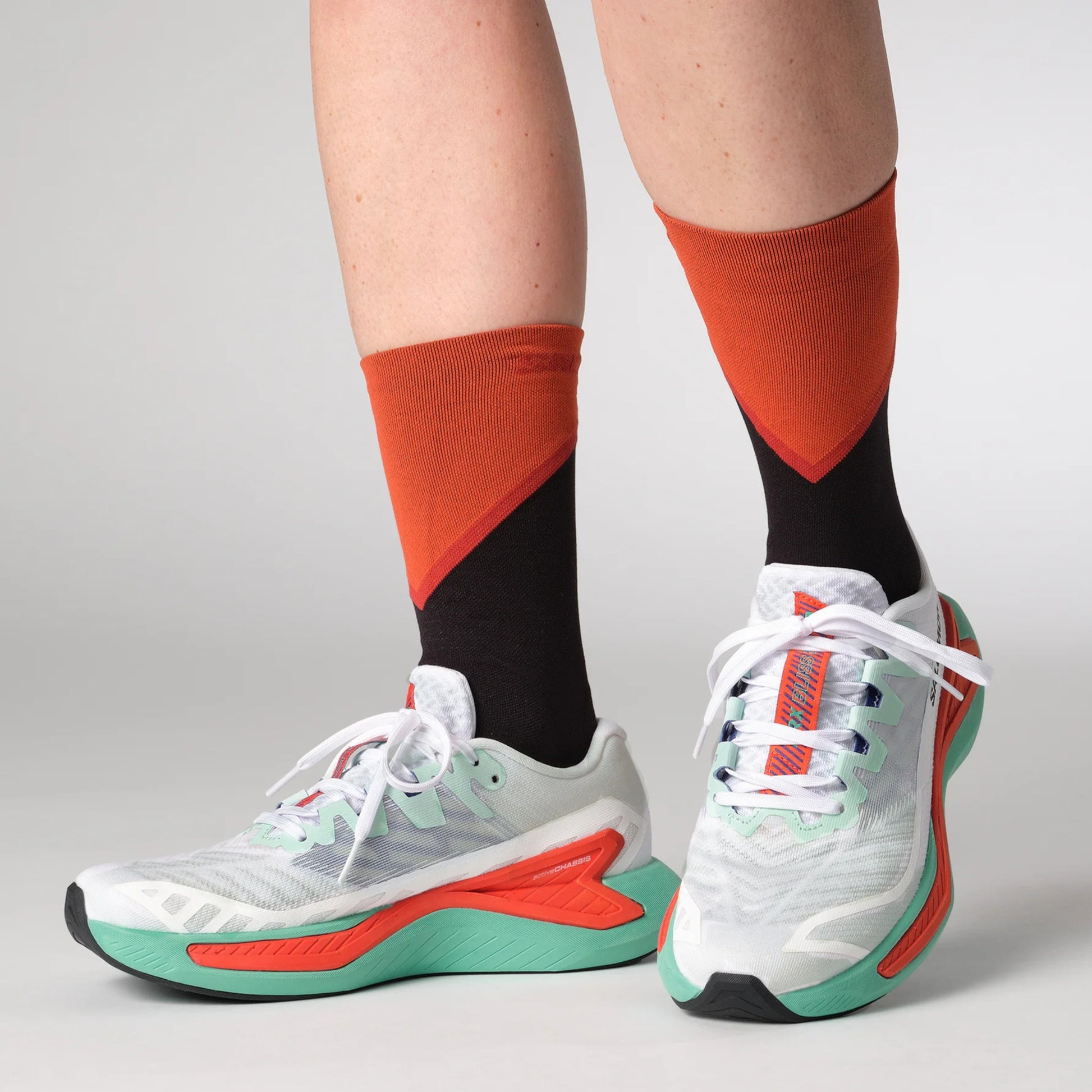 White running shoes with red and green accents worn with orange and black socks on a light gray background