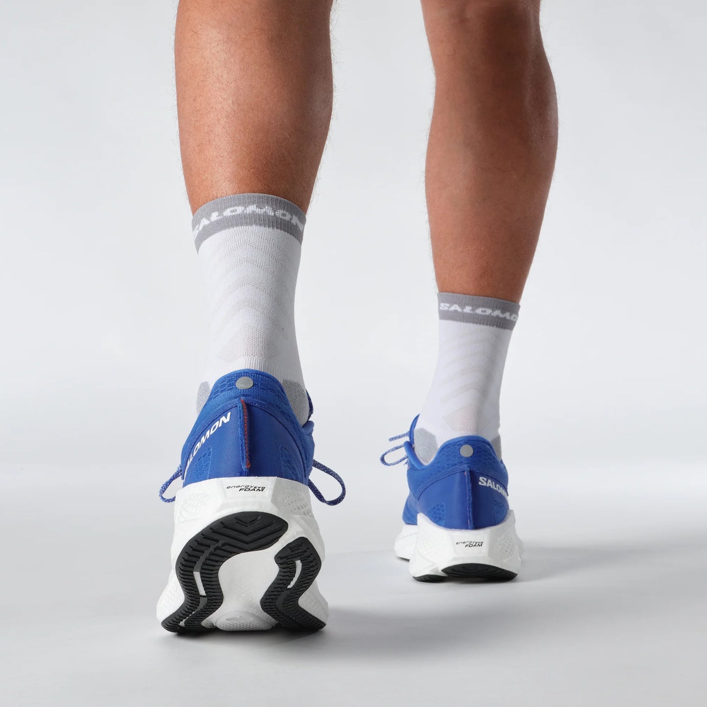 Person wearing Salomon blue running shoes and white socks with visible brand logos on a light gray background