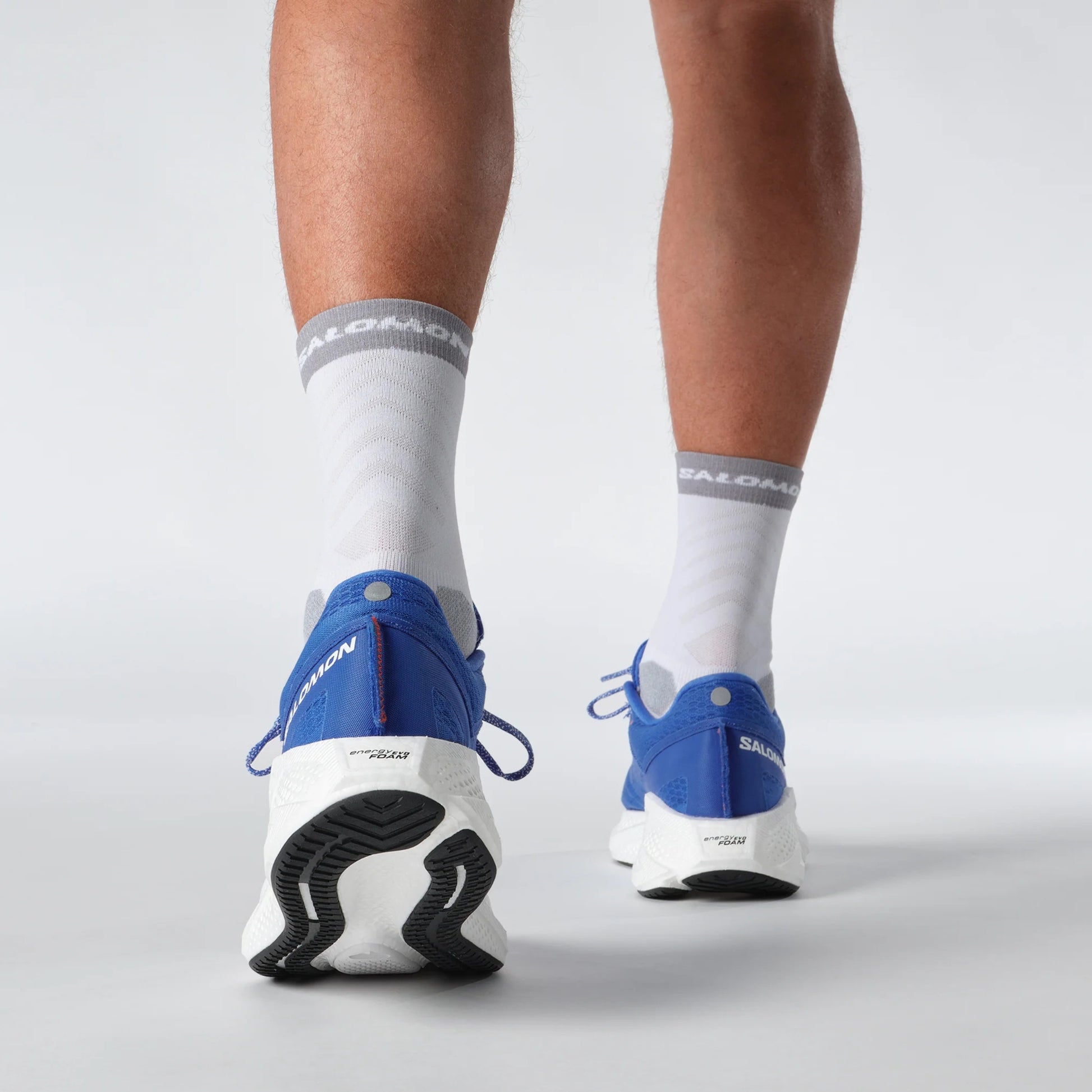 Person wearing Salomon blue running shoes and white socks with visible brand logos on a light gray background