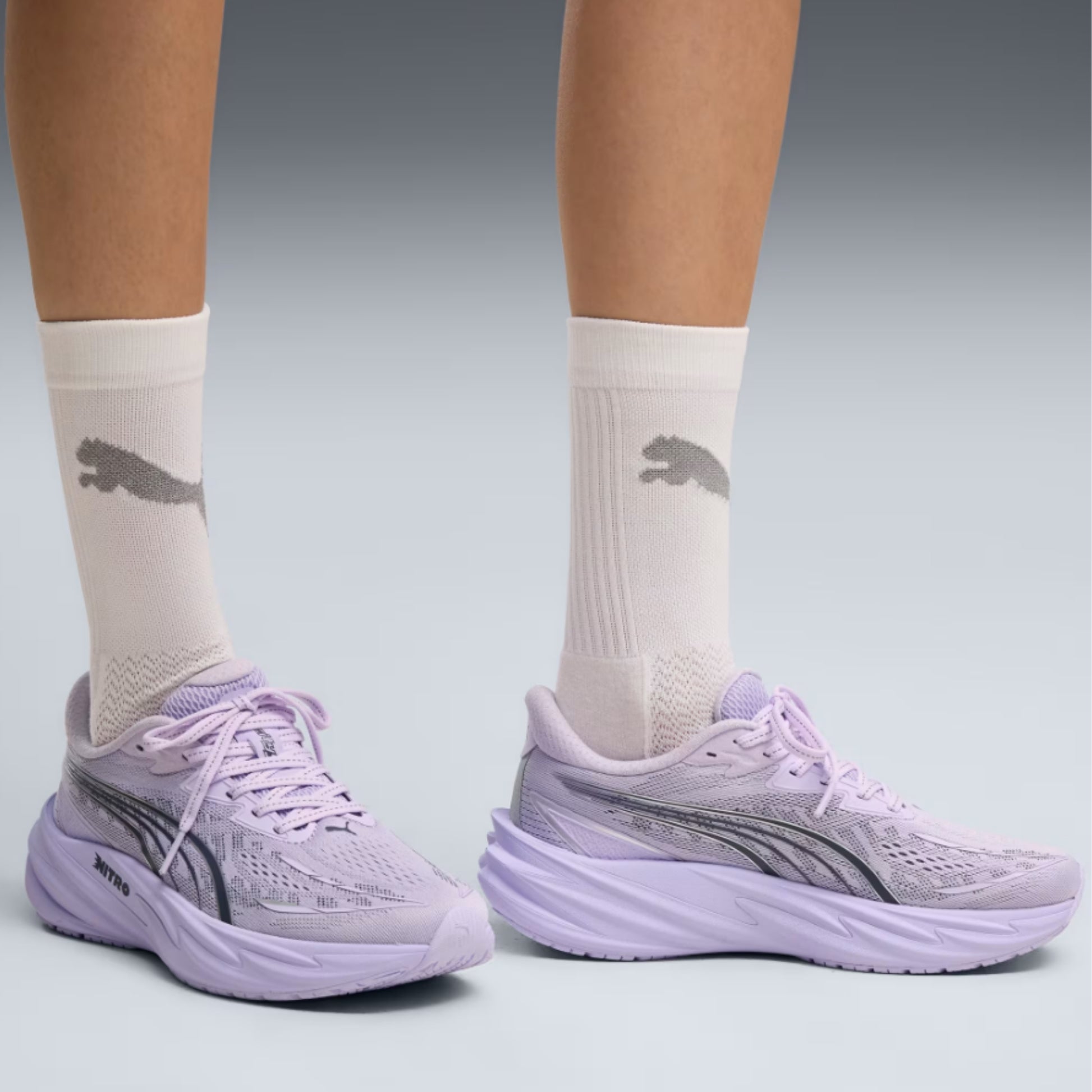 A person wearing light purple Puma running shoes with matching purple socks, shown from the calves down against a light gray studio background.