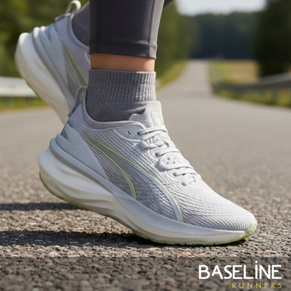 Person wearing light gray Puma running shoes on a road with 'Baseline Runners' branding.