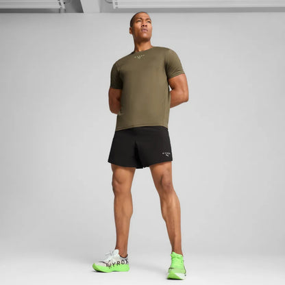 Man wearing an olive green t-shirt and black shorts with neon green shoes on a gray background