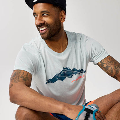 Man wearing a white t-shirt with a logo, sitting against a plain background