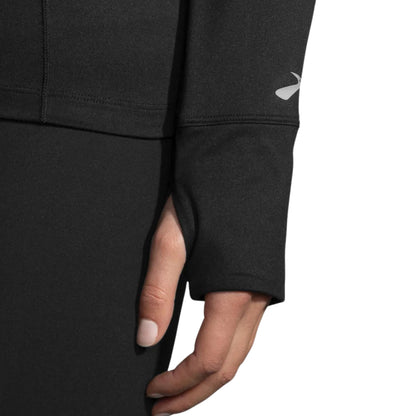 Close-up of a woman wearing a black Brooks jersey, focusing on the wrist with clothing peace over her thumb on a white background