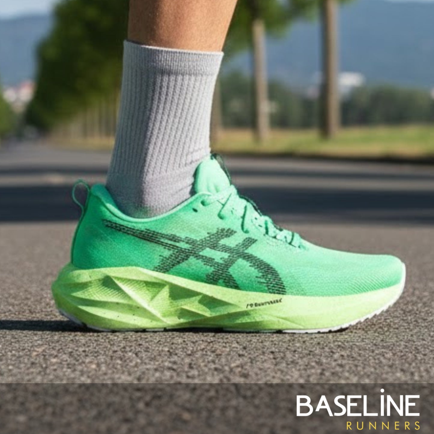 Green Asics running shoe worn on a road with blurred background