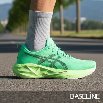 Green Asics running shoe worn on a road with blurred background