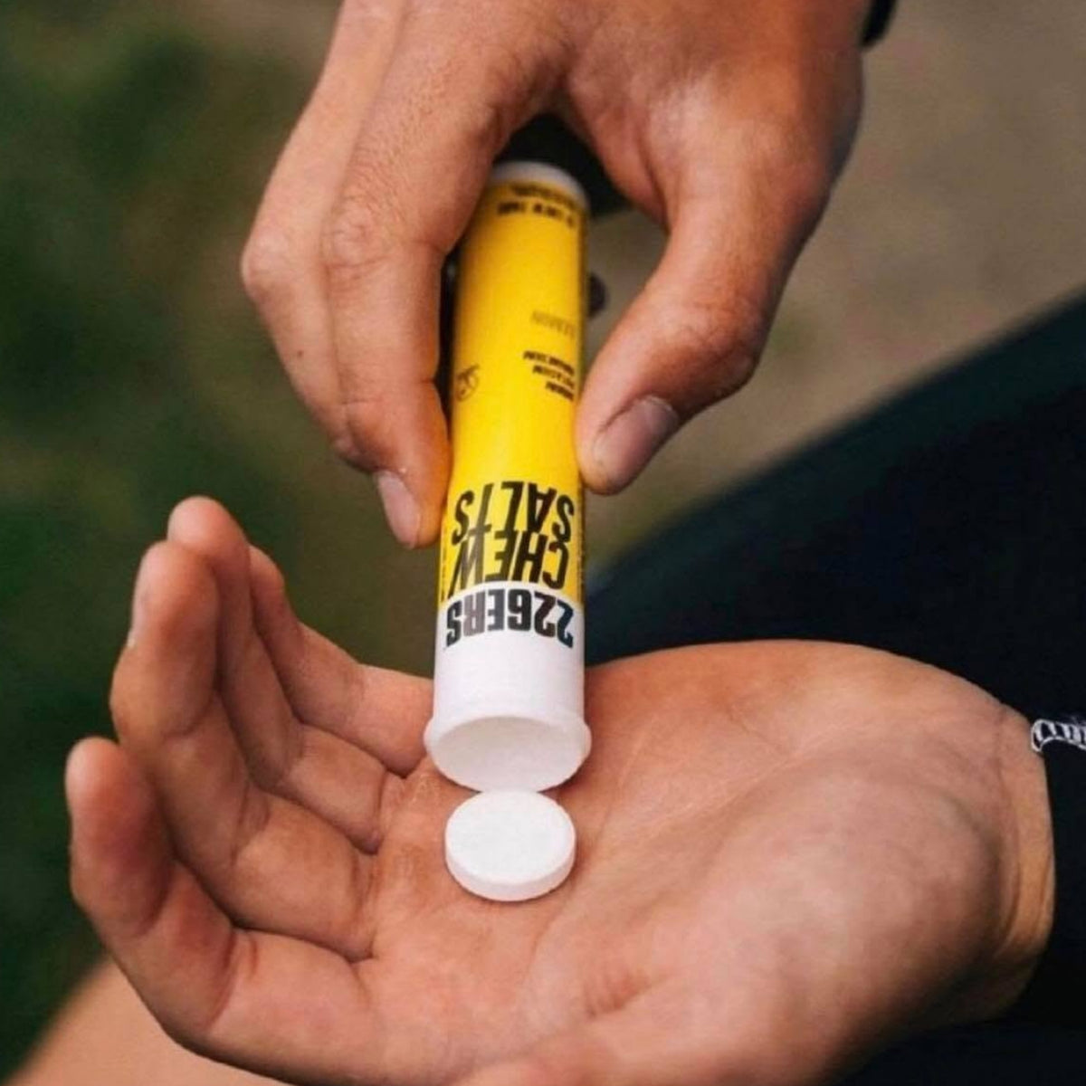 A close-up of a person's hands squeezing a yellow and white tube labeled '226ERS CHEW SALTS' into their palm, with a single white chewable tablet resting below the open cap.