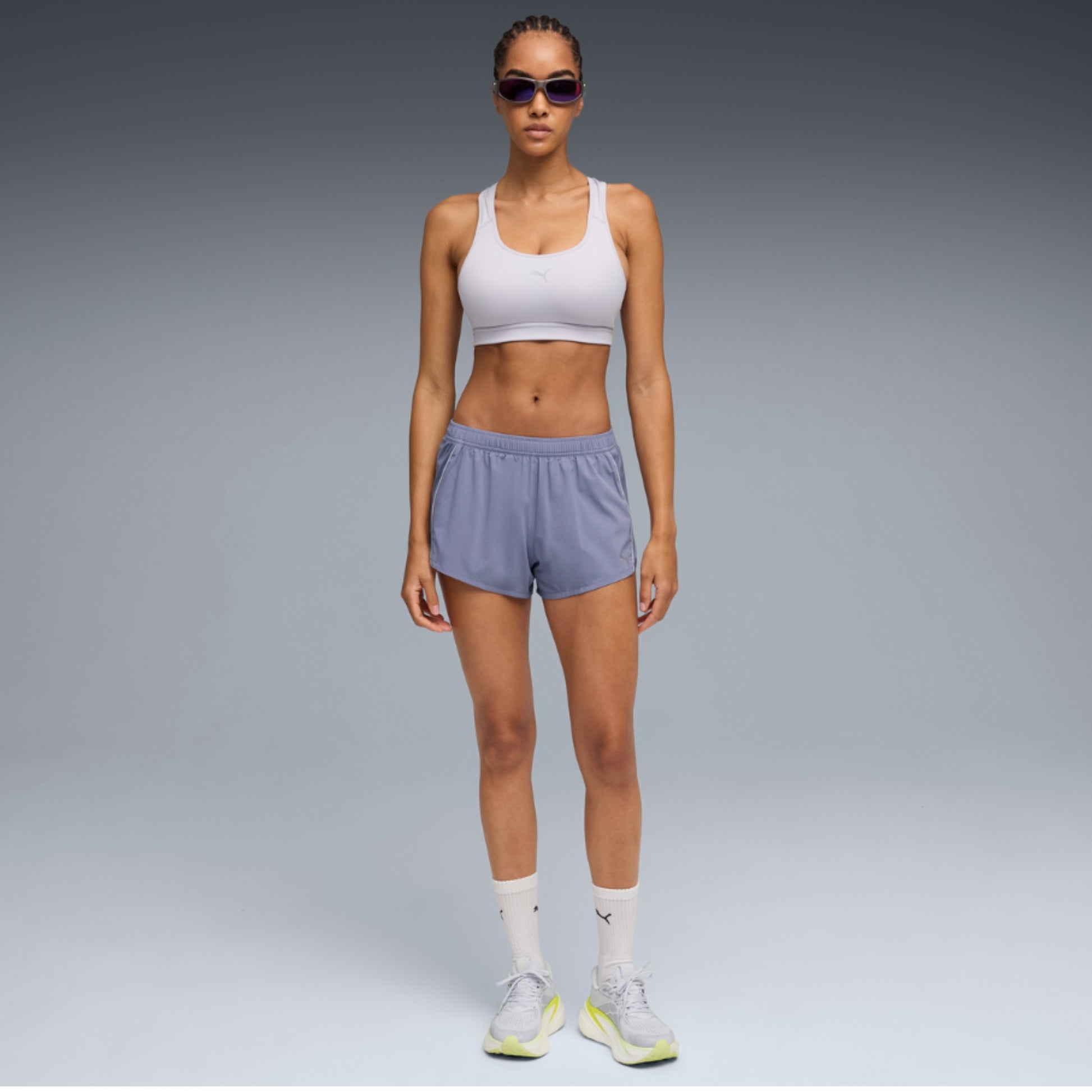 Woman wearing a white Puma sports bra and gray shorts on a white background