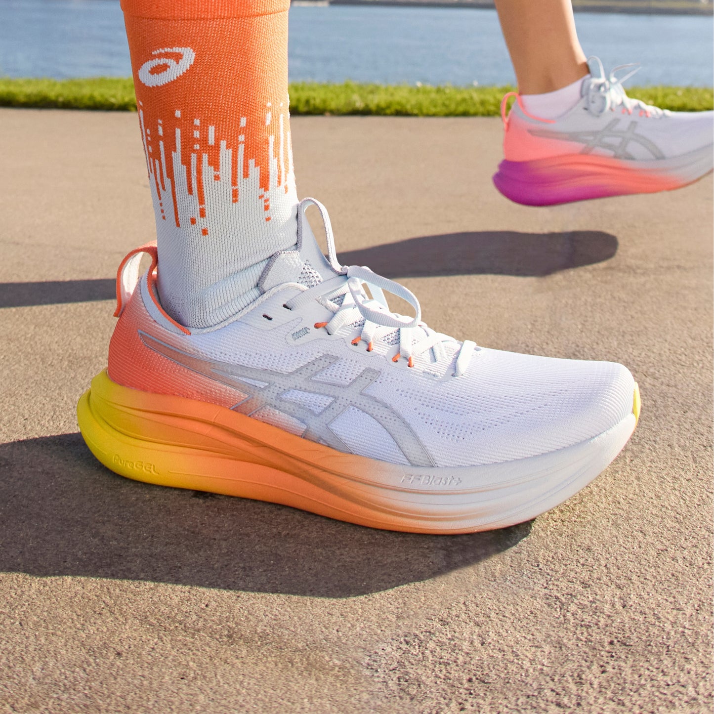 Person wearing white and orange Asics running shoe on a road background