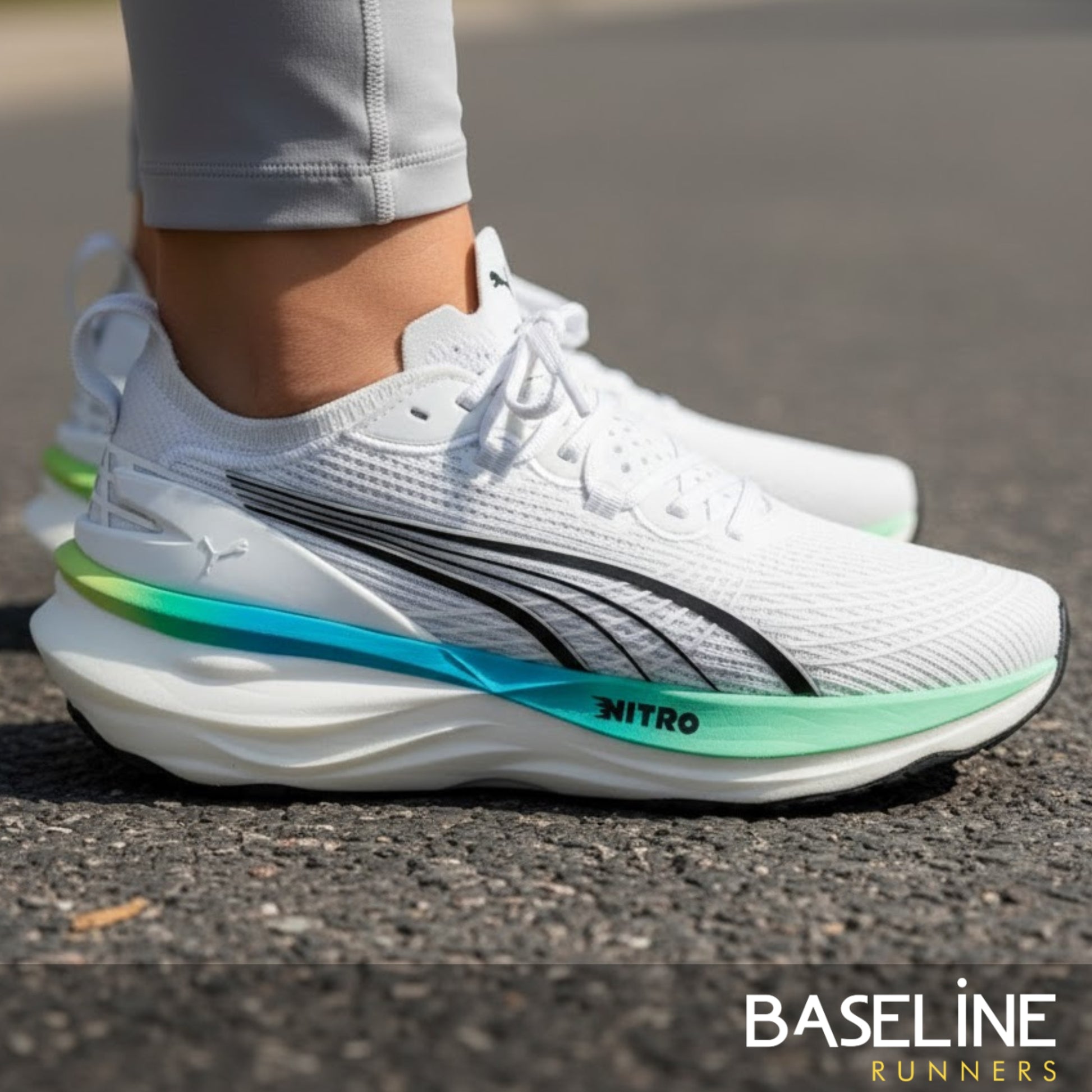 White running shoe with a blue and green sole on a road, featuring the brand 'Puma'.