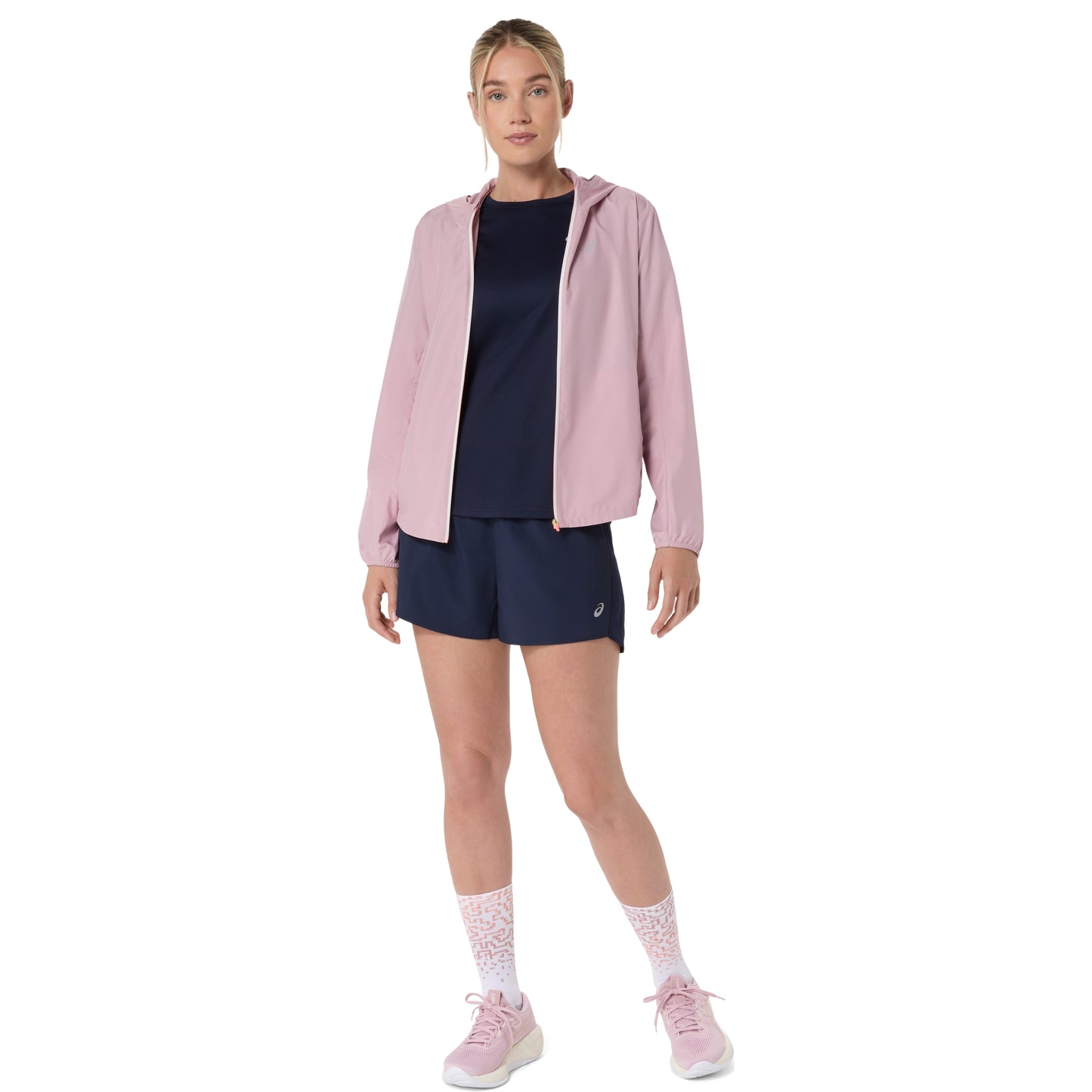 Woman wearing a pink jacket, navy outfit, and pink shoes on a white background