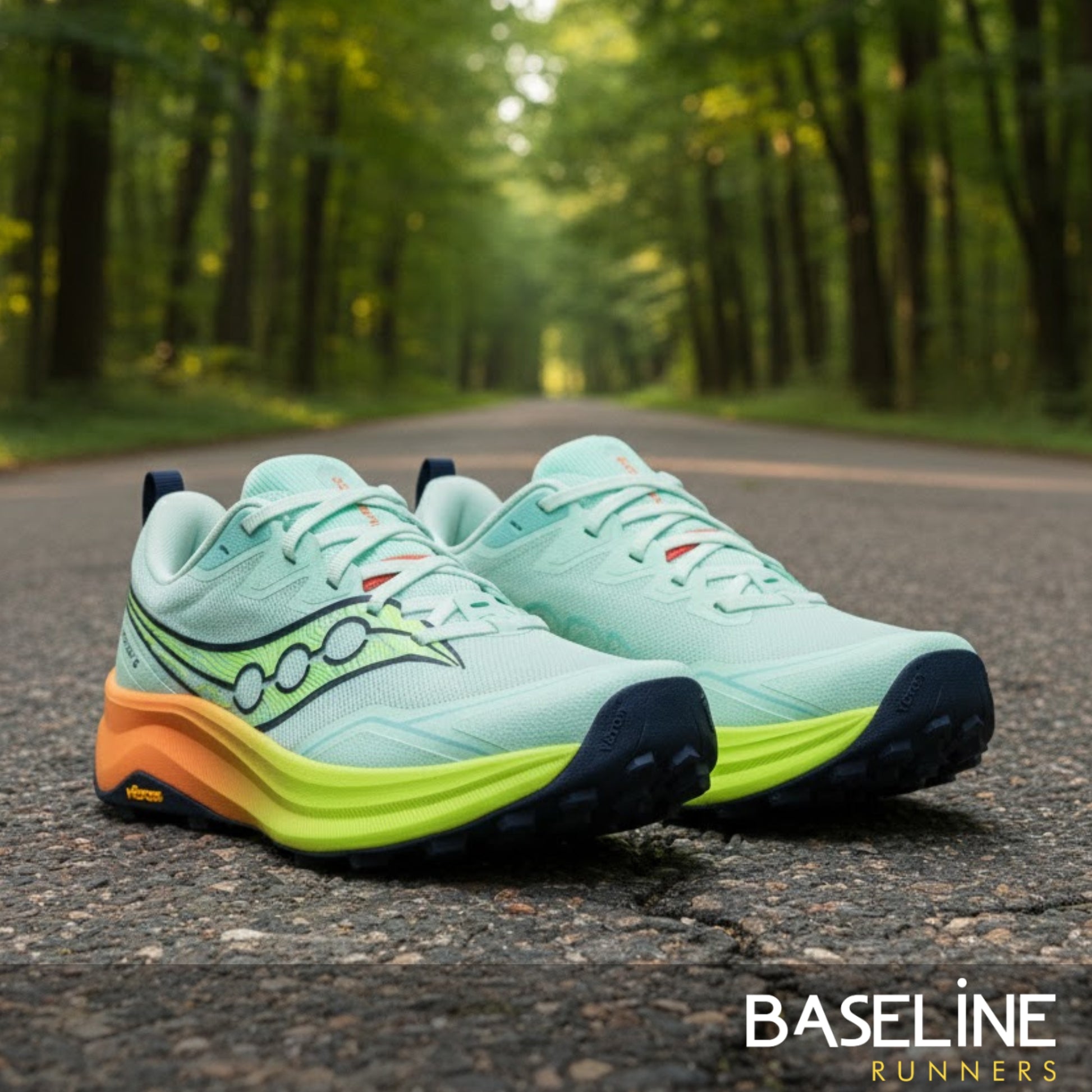 Pair of light blue running shoes with orange and green sole on a road in a forest.
