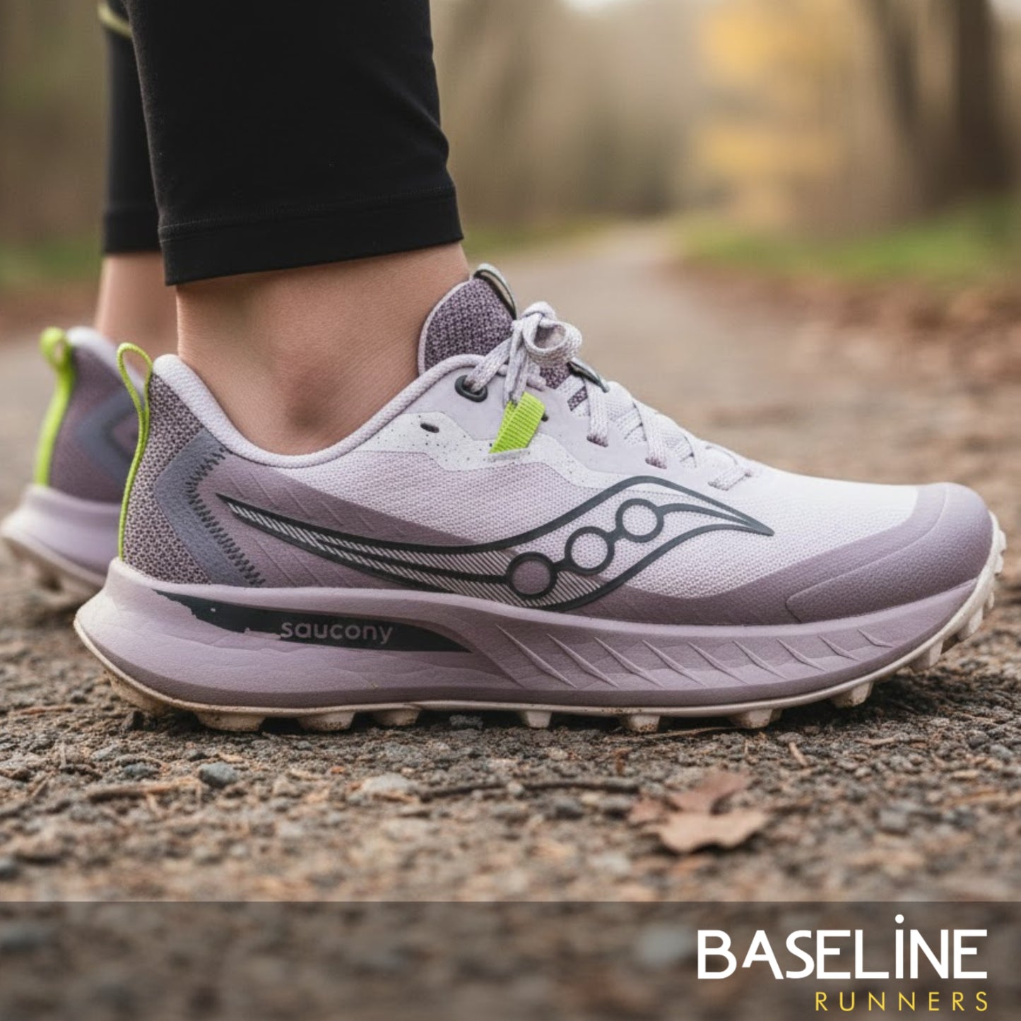 Purple and light purple running shoe with green accents on a blurred natural background, featuring the Saucony brand.