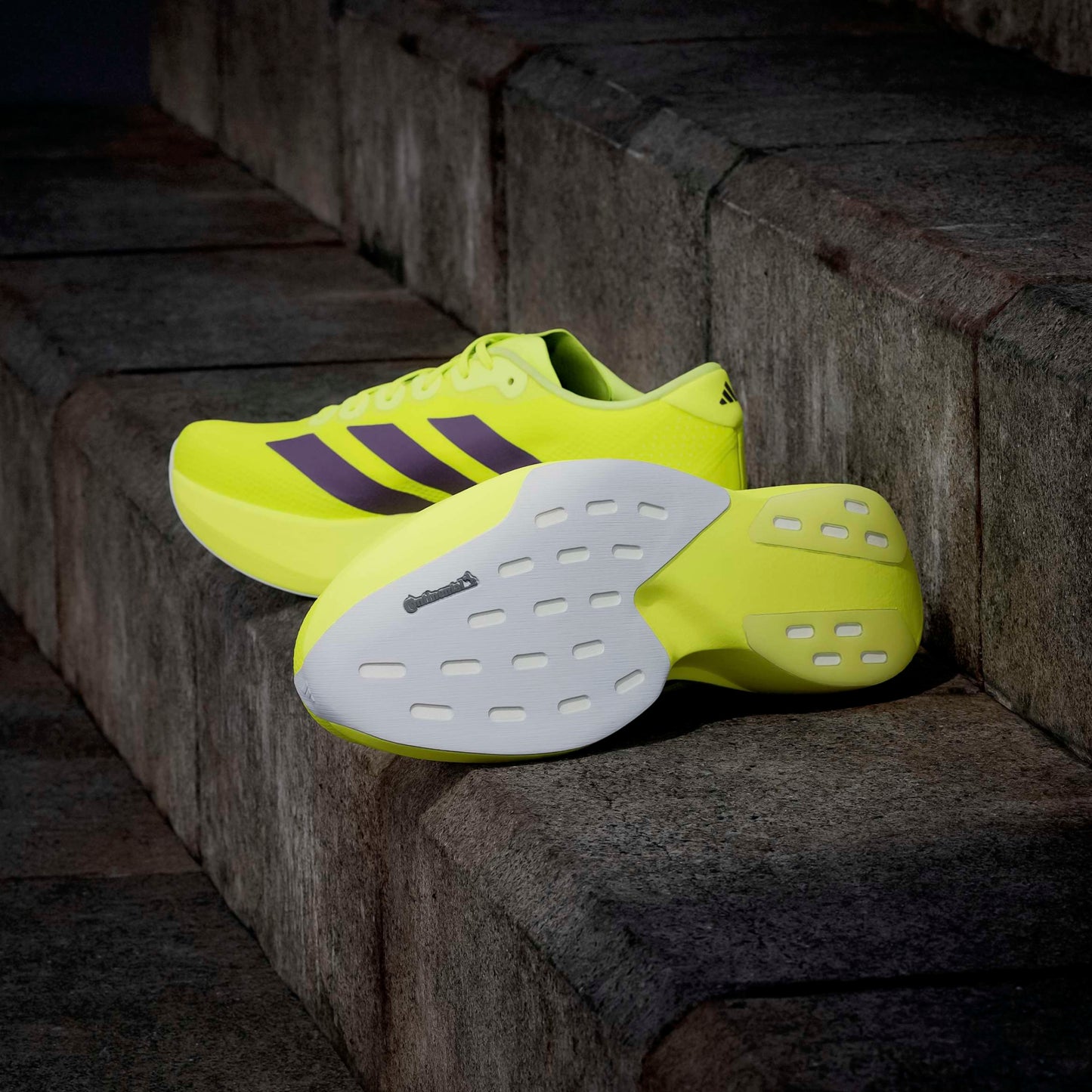 Bright yellow adidas running shoes with white soles on a stone step