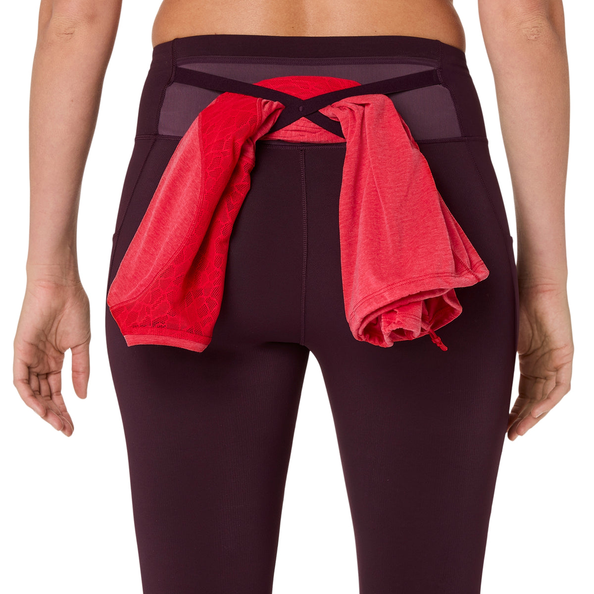Rear view of a model wearing dark plum leggings with a red athletic shirt tied around the back waistband.
